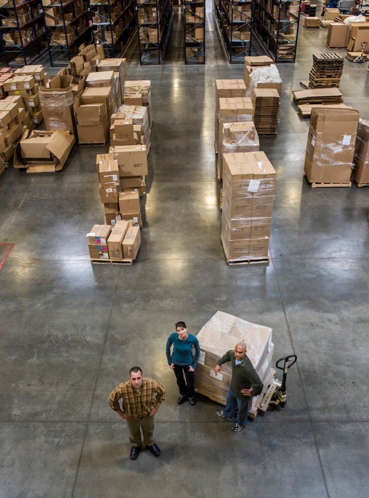 A group of three warehouse workers standing in the center of a distirbution warehouse. A group of three warehouse workers standing in the center of a distirbution warehouse.