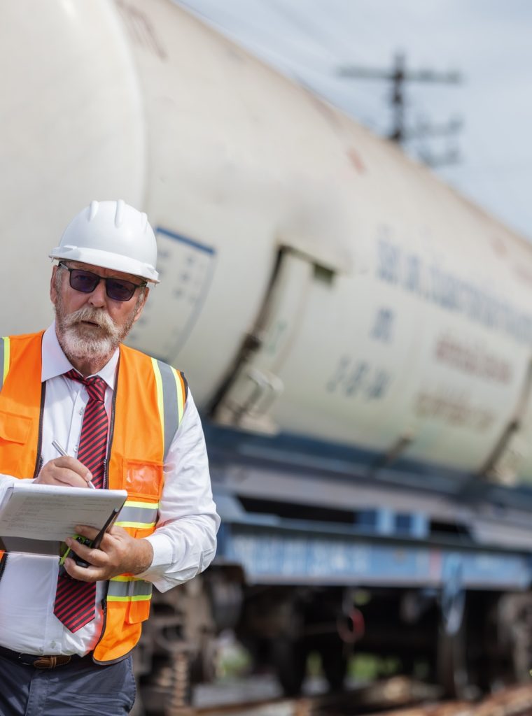 A senior engineer in safety gear takes notes during an inspection of a chemical tank railcar. A senior engineer in safety gear takes notes during an inspection of a chemical tank railcar.