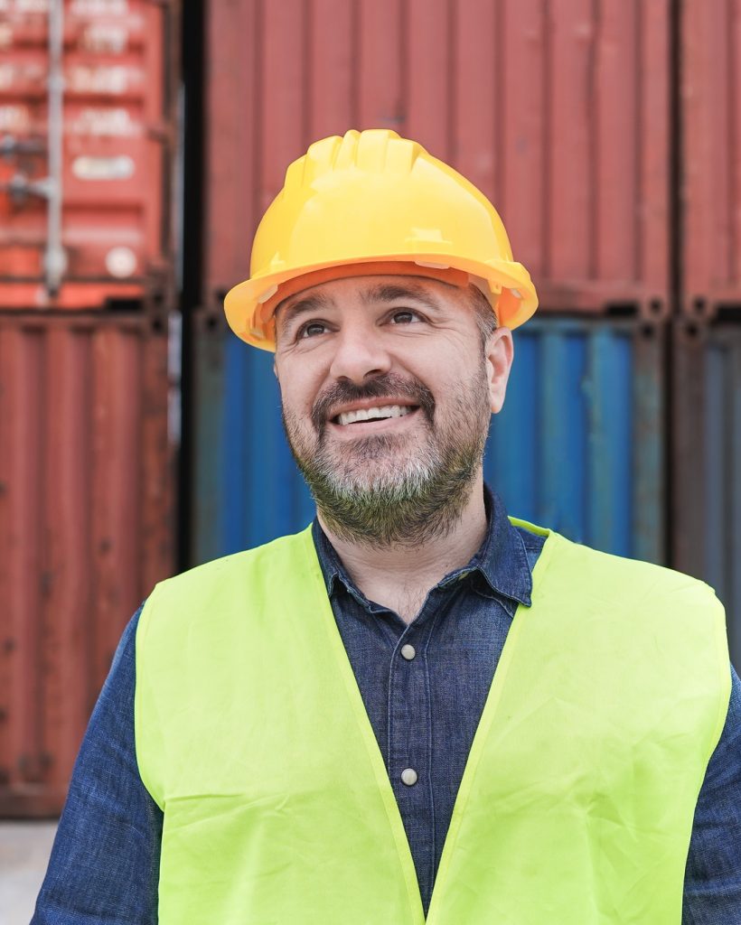 Professional dock worker wearing hardhat and safety vest standing at container yard port